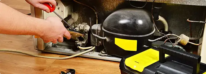 Refrigerator repair technician fixing the compressor and wiring in Yoder, IN