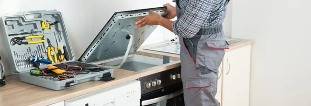 Cooktop repair technician lifting a built-in stovetop for service in Fort Wayne, IN
