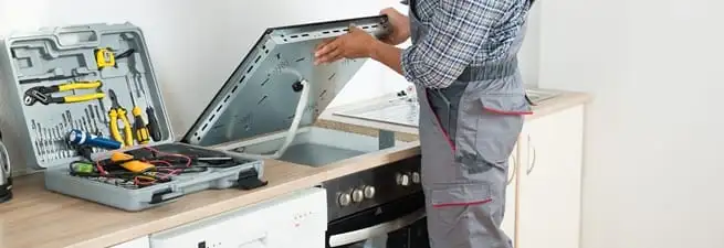 Cooktop repair technician lifting a built-in stovetop for service in Fort Wayne, IN