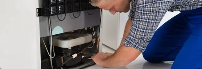 Refrigerator repair technician servicing the compressor and condenser area in Fort Wayne, IN