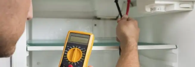 Refrigerator repair technician testing electrical components with a multimeter in Fort Wayne, IN