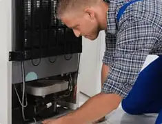 Refrigerator repair technician servicing the compressor and condenser area in Fort Wayne, IN